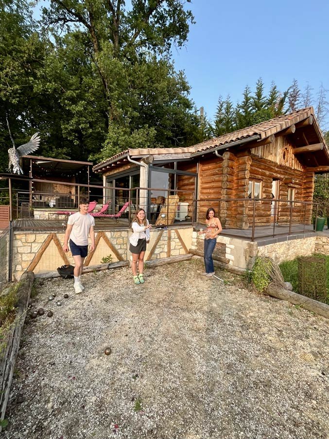 Partie de pétanque conviviale devant la Cabane de Rêve Trois personnes jouant à la pétanque devant le chalet en bois en fin de journée